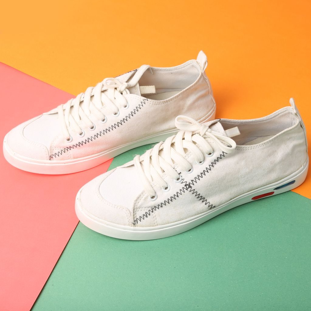 A pair of white canvas sneakers on a three color backdrop